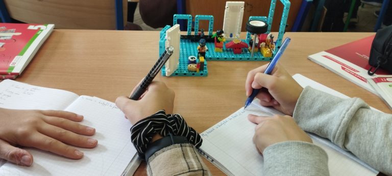 dłonie z długopisami, w tle klocki lego