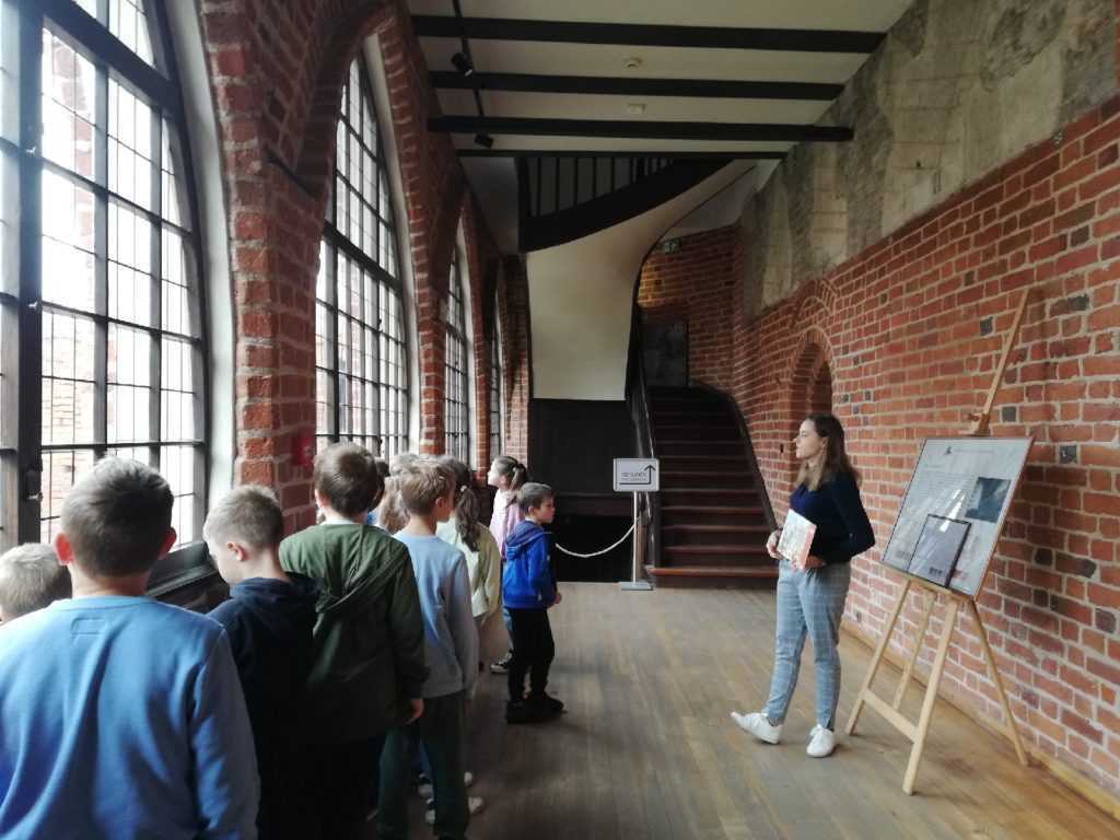 uczniowie słuchający przewodnika na zamkowym korytarzu