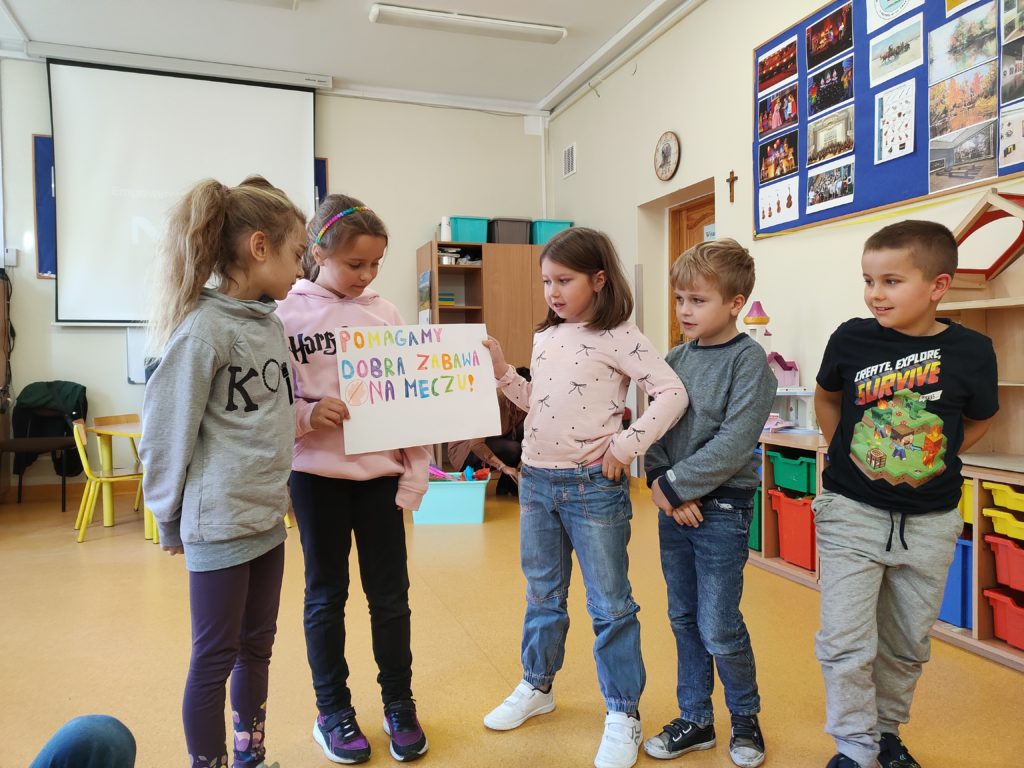 dzieci stojące, przedstawiające swoją grę planszową