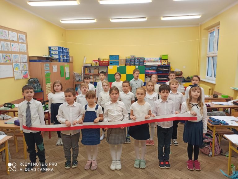 uczniowie w strojach galowych śpiewają hymn w klasie