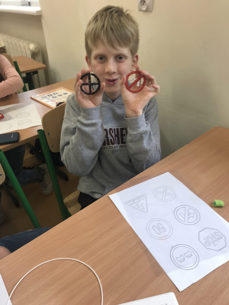 uczeń trzyma w ręku dwa znaki zrobione za pomocą dugopisu 3D