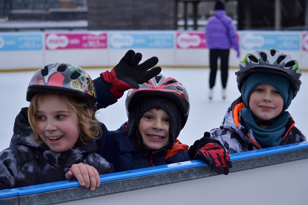 Troje uczniów w kaskach opartych o barierę lodowiska