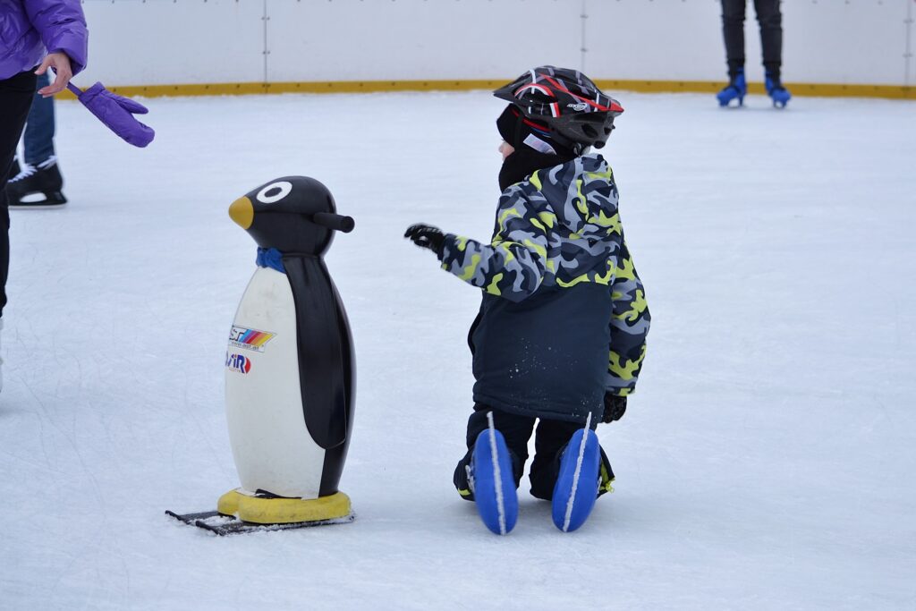 Dziecko odwrócone tyłem łapie się pingwinka na lodowisku