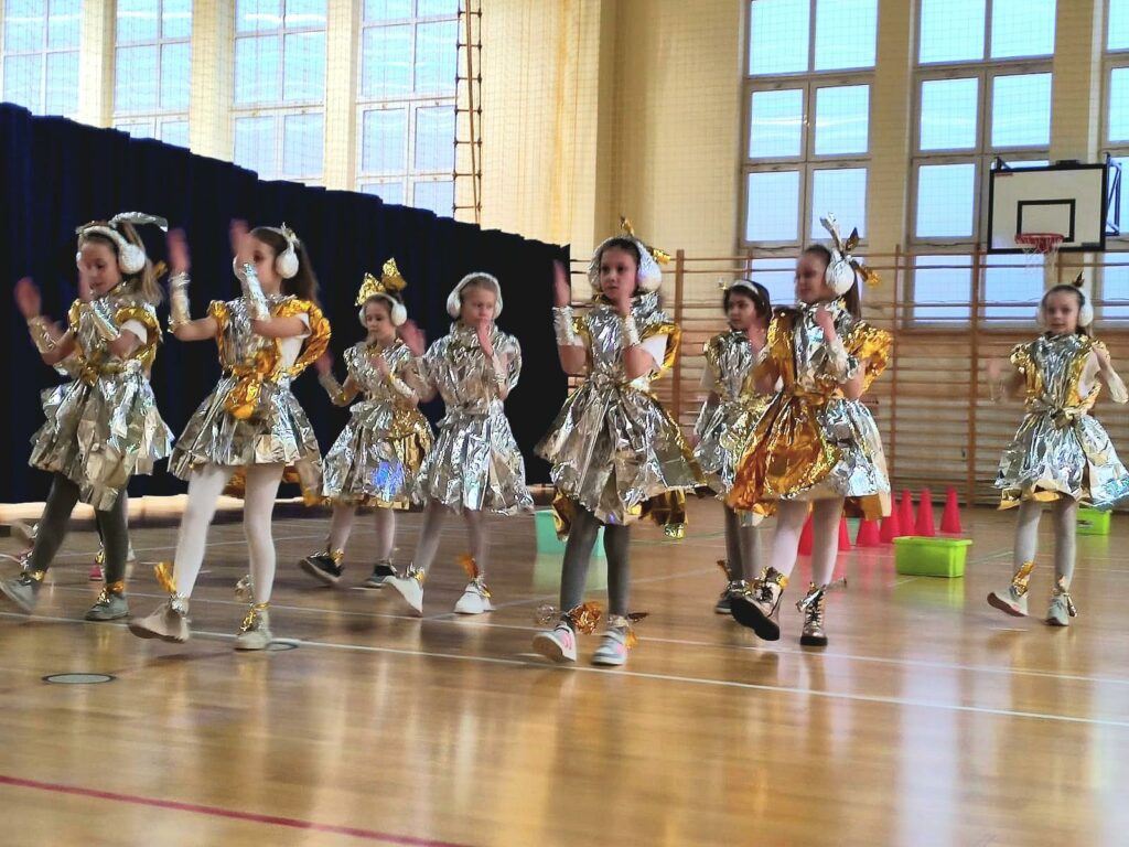 Osiem dziewczynek, ubranych w metaliczne sukienki, przypominające folie aluminiowe, tańczą układ taneczny. Naśladując przy tym przybyszów z obcej planety.