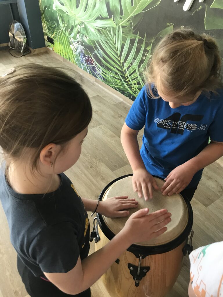 Dzieci – chłopiec i dziewczynka, stoją przy afrykańskich bębnach. Uderzają dłońmi o kongi.