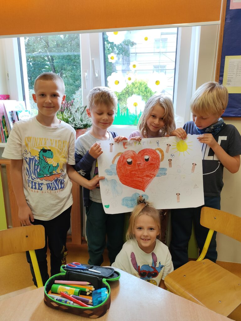 trzech chłopców i dwie dziewczynki trzymają plakat na którym narysowane jest duże czerwone serce i napis empatia