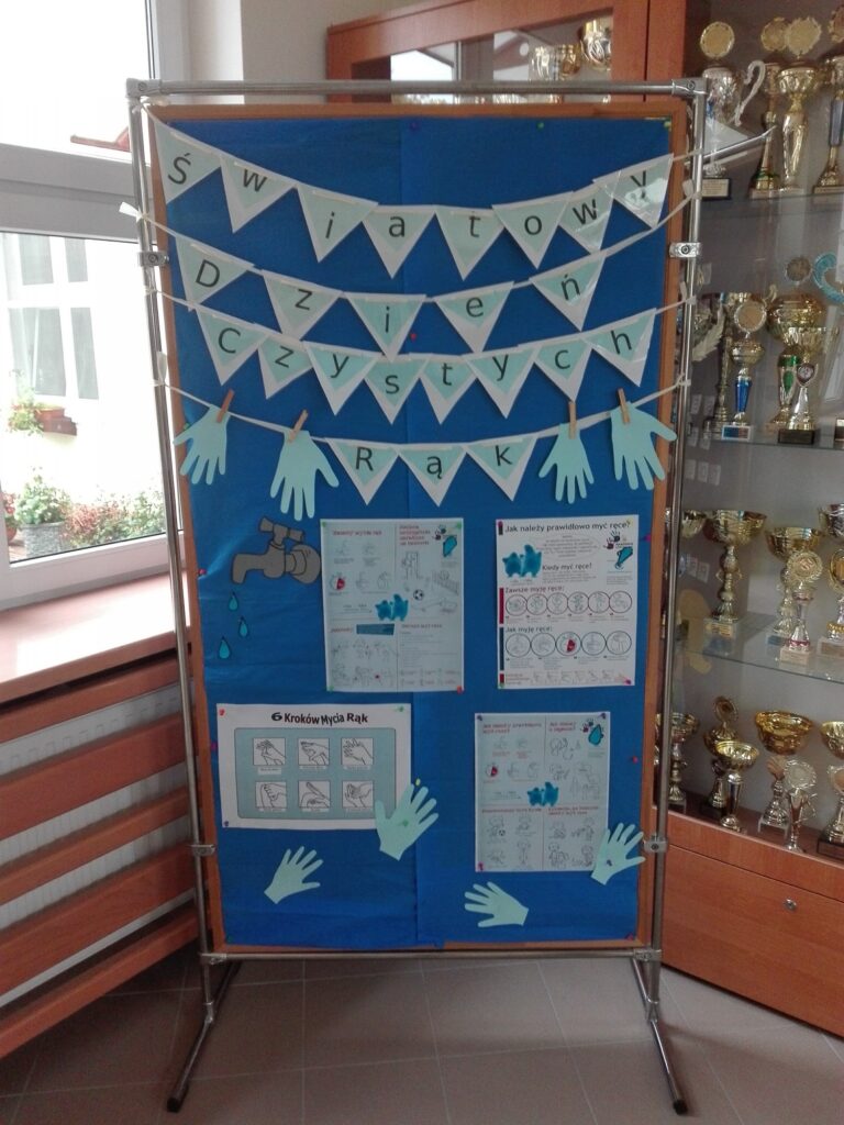 Na zdjęciu znajduje się tablica informacyjna na temat higieny rąk. Jest to pionowa tablica. Na granatowym tle przyczepione są jasnoniebieskie kartki z informacjami