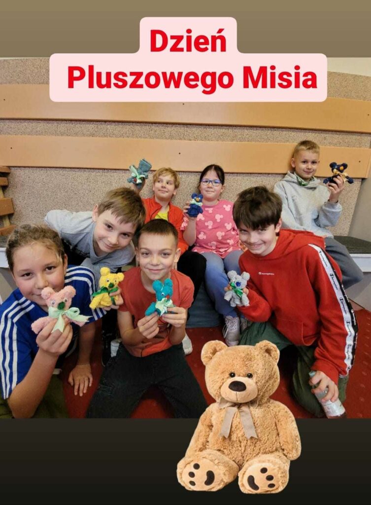 Na zdj臋ciu wida膰 na tle szarej 艣ciany 7 dzieci trzymaj膮cych w r臋kach r贸偶nokolorowe misie zrobione z ma艂ych r臋cznik贸w. Na g贸rze zdj臋cia widnieje napis "Dzie艅 Pluszowego Misia". W dole zdj臋cia obecna jest grafika misia.