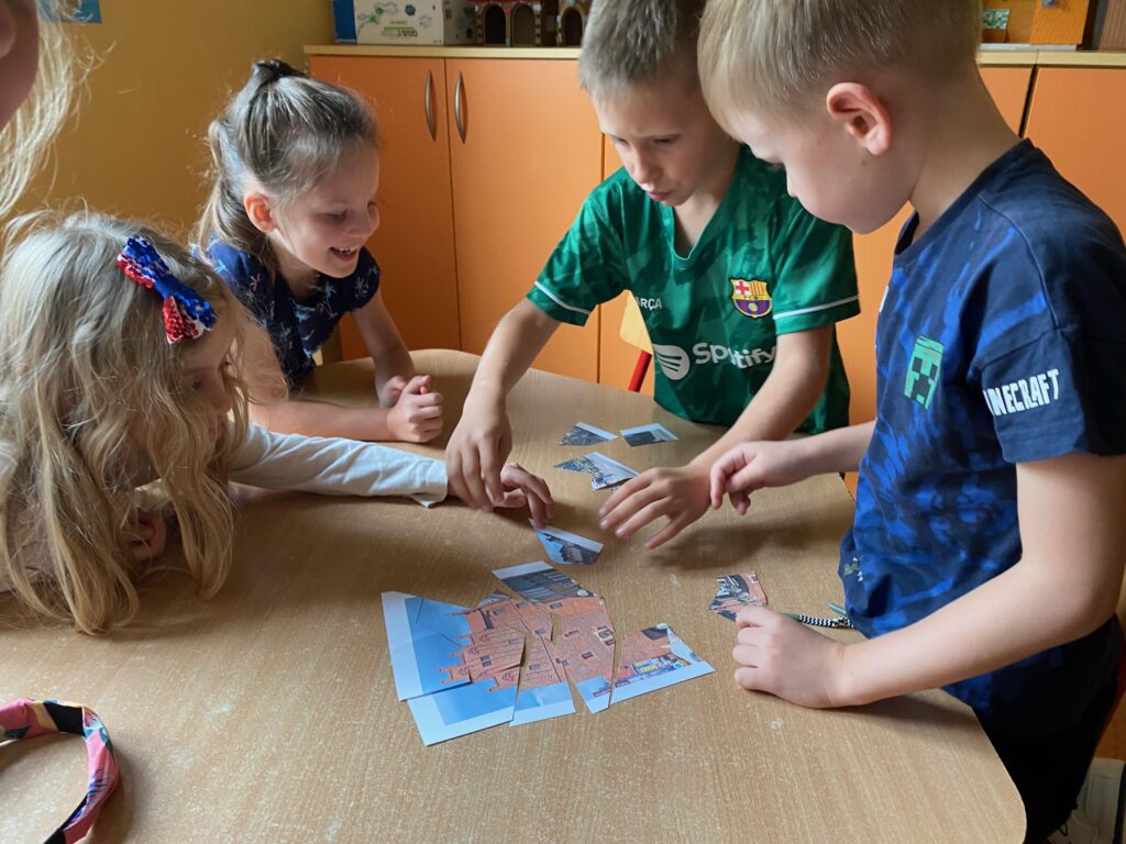 Dzieci przy stoliku wspólnie układają puzzle z zabytkami Olsztyna.