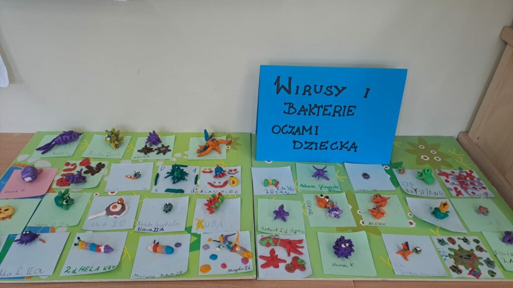 Wystawa prac dzieci „Wirusy i bakterie oczami dziecka”. Widać mnóstwo kolorowych figurek bakterii i wirusów zrobionych z plasteliny na zielonym tle.