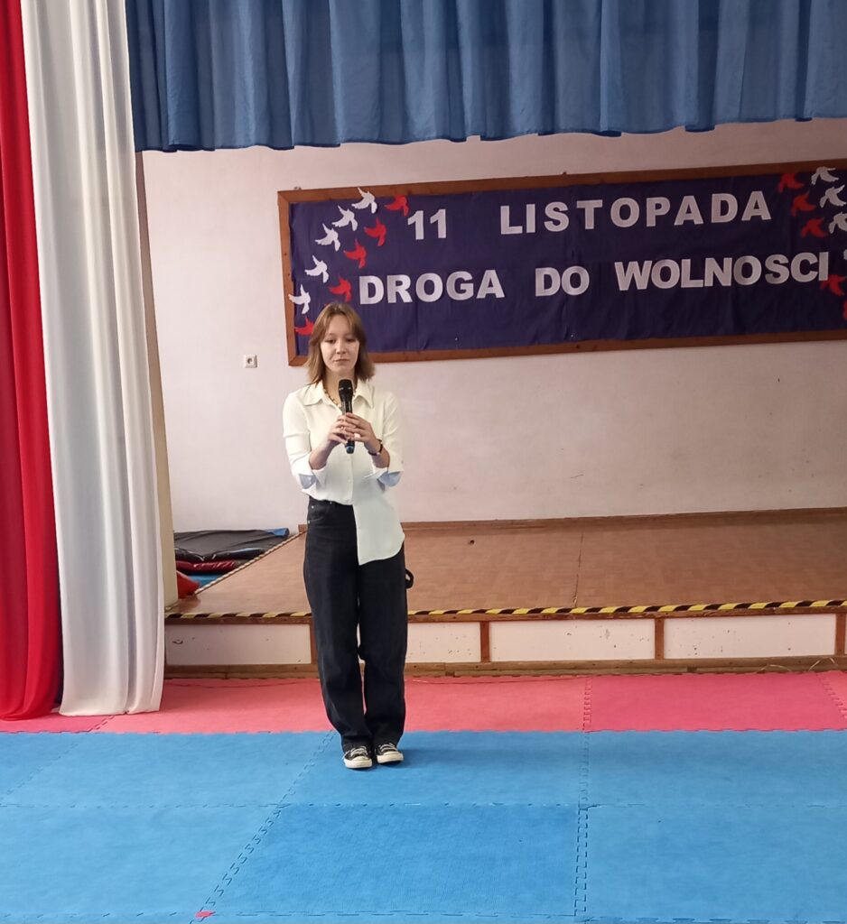 na środku dziewczynka w stroju galowym, w skupieniu trzymająca mikrofon