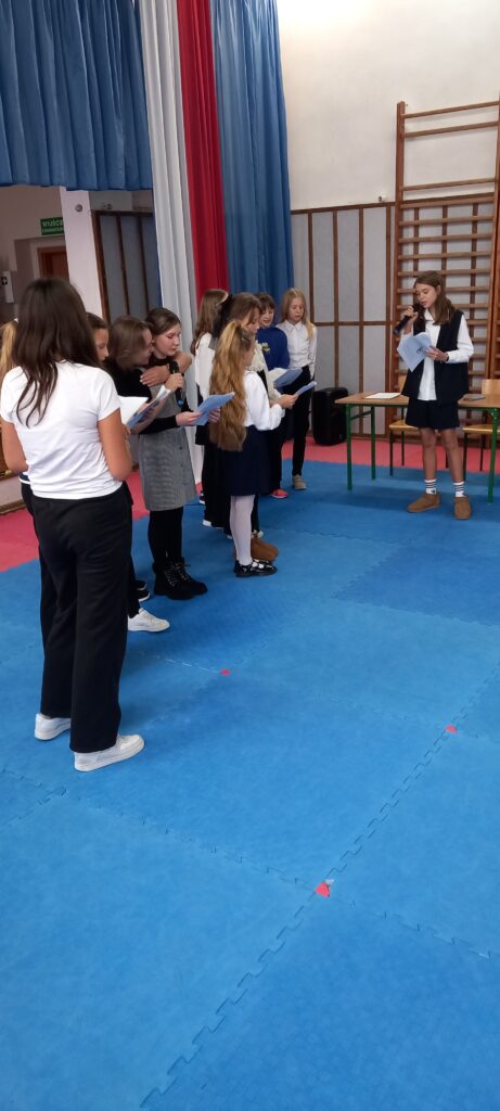 wszystkie uczestniczki wraz z jurorką - przedstawicielką uczniów szkoły - śpiewają pieść patriotyczną. Trzymają śpiewniki z tekstem.