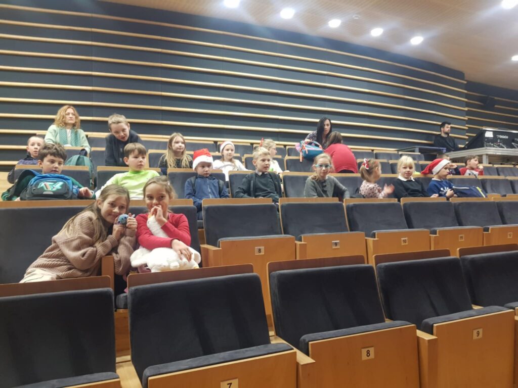 Na duzej sali koncertowej, na widowni, siedzi grupa dzieci.