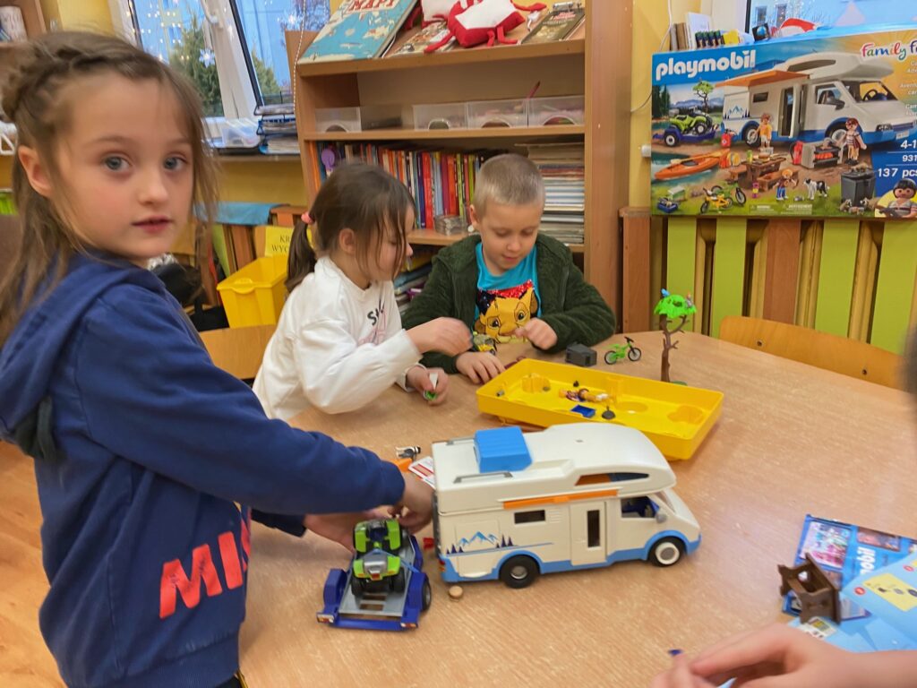 Dzieci przy stolikach bawiące się zabawkami od Św. Mikołaja- zestawy Play Mobil.