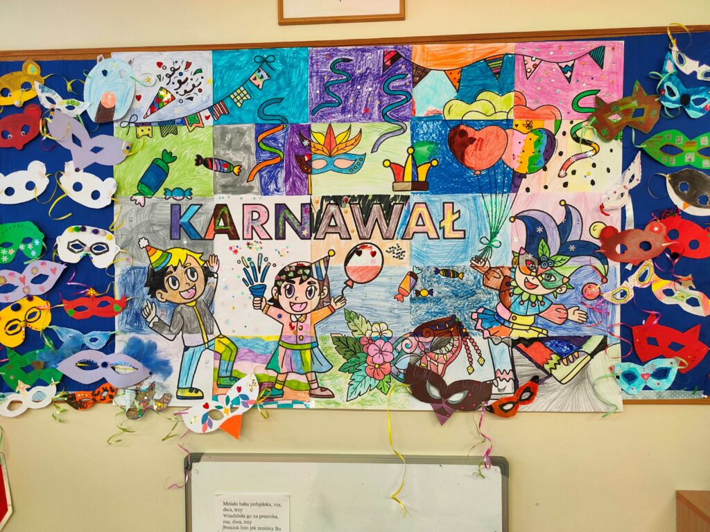 Na zdjęciu widzimy kolorową tablicę dekoracyjną z motywem karnawałowym. Centralnym elementem jest duży rysunek przedstawiający postacie w karnawałowych strojach, otoczone balonami, serpentynami i konfetti. Wokół rysunku przymocowano wiele ozdobnych masek wykonanych z papieru, w różnych kształtach i kolorach. Całość tworzy radosną, pełną barw kompozycję nawiązującą do atmosfery zabawy karnawałowej.