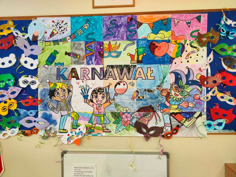 Na zdjęciu widzimy kolorową tablicę dekoracyjną z motywem karnawałowym. Centralnym elementem jest duży rysunek przedstawiający postacie w karnawałowych strojach, otoczone balonami, serpentynami i konfetti. Wokół rysunku przymocowano wiele ozdobnych masek wykonanych z papieru, w różnych kształtach i kolorach. Całość tworzy radosną, pełną barw kompozycję nawiązującą do atmosfery zabawy karnawałowej.