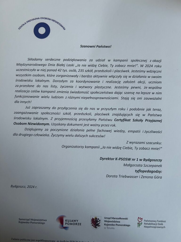 Zdjęcie przedstawia oficjalne podziękowanie za udział w kampanii społecznej „Ja nie widzę Ciebie, Ty zobacz mnie!”, organizowanej z okazji Międzynarodowego Dnia Białej Laski. Dokument został wydany przez Kujawsko-Pomorski Specjalny Ośrodek Szkolno-Wychowawczy nr 1 w Bydgoszczy i podpisany przez jego dyrektora Małgorzatę Szczepanek oraz tyflopedagogów Dorotę Triebwasser i Zenonę Góra. Podziękowanie zawiera informacje, że w kampanii w 2024 roku uczestniczyło ponad 42 tysiące osób, 235 szkół, przedszkoli i placówek. Organizatorzy wyrażają wdzięczność za zaangażowanie w działania na rzecz osób niewidomych oraz podkreślają wpływ kampanii na zmianę świadomości społecznej i poprawę warunków życia osób z niepełnosprawnościami. Dokument zachęca do ponownego udziału w przyszłych edycjach kampanii i informuje, że w ramach podziękowania szkoła otrzymuje Certyfikat Szkoły Przyjaznej Osobom Niewidomym, ważny przez rok. Na dole strony znajdują się logotypy instytucji wspierających kampanię, takich jak: • Samorząd Województwa Kujawsko-Pomorskiego, • Urząd Marszałkowski Województwa Kujawsko-Pomorskiego w Toruniu, • Państwowy Fundusz Rehabilitacji Osób Niepełnosprawnych (PFRON), • Kujawy Pomorze. Treść dokumentu jest wydrukowana na białym tle, z niebieskimi i czarnymi napisami. W lewym górnym rogu znajduje się logo kampanii „Szkoła Przyjazna Osobom Niewidomym”, przedstawiające okrągły symbol w kolorze niebieskim.
