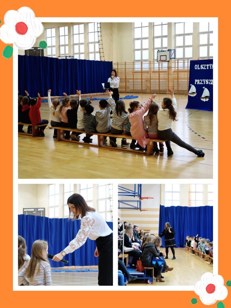 Zdjęcie przedstawia szkolne wydarzenie w sali gimnastycznej, gdzie dzieci aktywnie biorą udział w spotkaniu. Prowadząca zadaje pytania, a uczniowie chętnie odpowiadają, podnosząc ręce. W tle widoczna jest dekoracja nawiązująca do przyszłych pierwszoklasistów. Na trybunach siedzą dorośli i dzieci, a całość ma ciepły, interaktywny charakter. Pomarańczowa ramka z kwiatami dodaje przyjaznego nastroju.