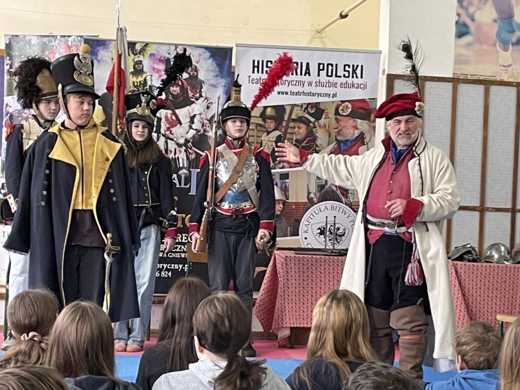 Stoi czworo uczniów w mundurach z pierwszej połowy XIX wieku.