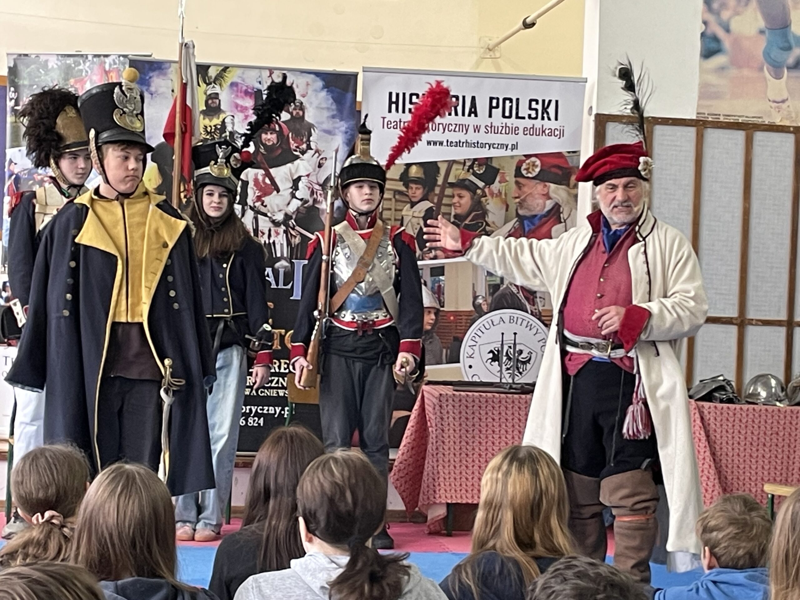 Stoi czworo uczniów w mundurach z pierwszej połowy XIX wieku.