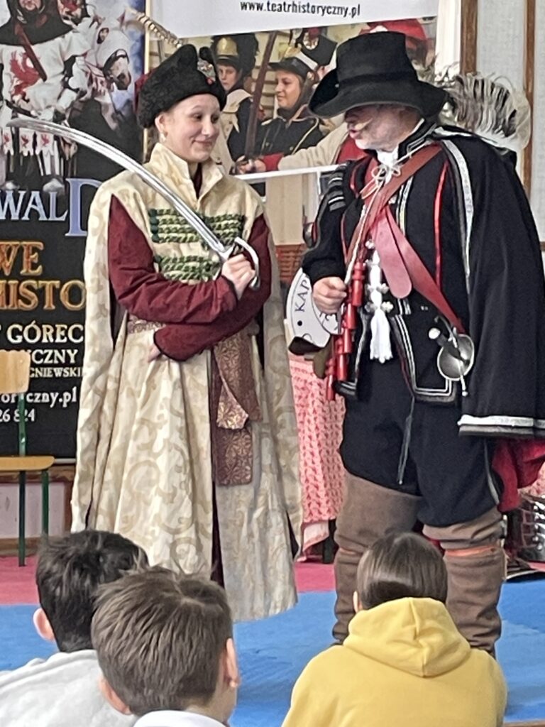 Na środku stoi dziewczyna przebrana w strój szlachcica.