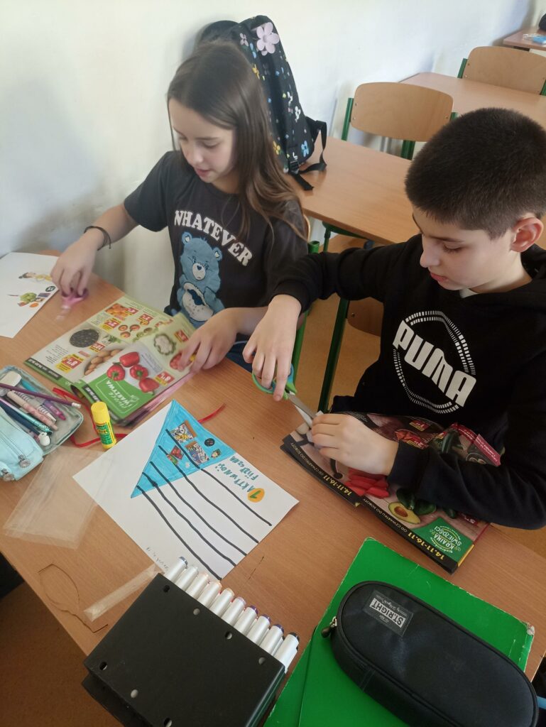 W centrum uwagi uczniów klasy 4c znajduje się gazetka, na której widać grupy produktów spożywczych, takie jak owoce, warzywa, zboża. Chłopiec wycina ilustracje przedstawiające grupy produktów spożywczych.