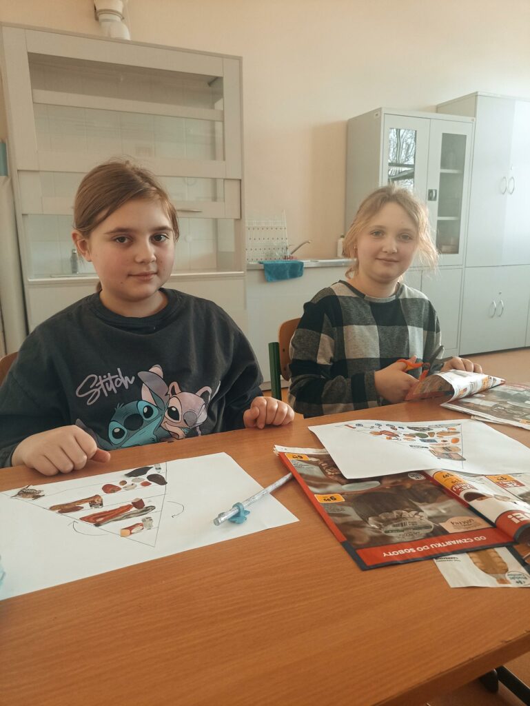 Na zdjęciu widzimy dziewczynki z klasy 4c siedzące w ławce podczas lekcji przyrody, które z zaangażowaniem tworzą własną piramidę zdrowego żywienia.