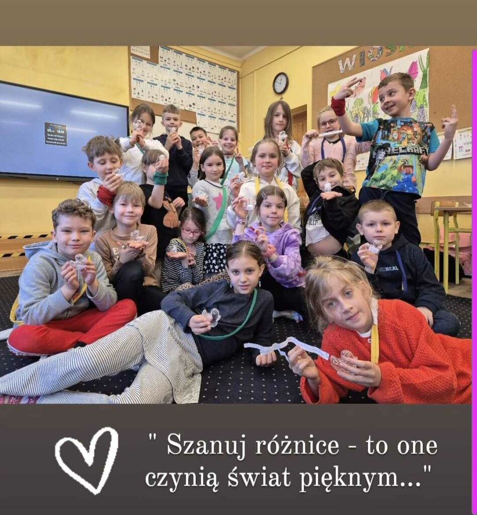 Zdjęcie przedstawia grupę dzieci, siedzących na dywanie i pozujących do zdjęcia. Na dole zdjęcia jest napisz "Szanuj różnice, to one czynią świat pięknym.