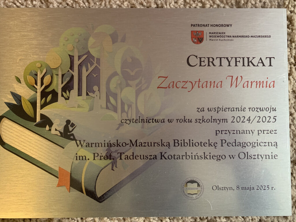 po prawej stronie widoczny jest napis CERTYFIKAT Zaczytana Warmia za wsparcie rozwoju czytelnictwa w roku szkolnym 2024/2025 przyznany przez Warmińsko-Mazurską Bibliotekę Pedagogiczną im. Prof. Tadeusza Kotarbińskiego w Olsztynie. Po lewej stronie widoczny jest rysunek leżącej książki, a z niej wyrastające drzewa