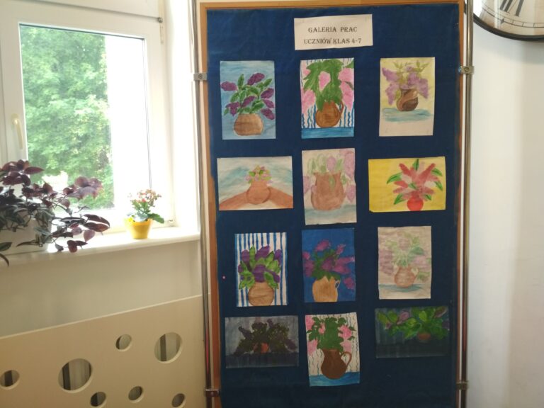 Zdjęcie przedstawia prace uczniów znajdujące się na tablicy, ustawione w pięciu rzędach po trzy prace, nad pracami znajduje się napis –galeria prac uczniów klas 4-7. Wszystkie prace przedstawiają prace z natury- liliowy bez w wazonie.