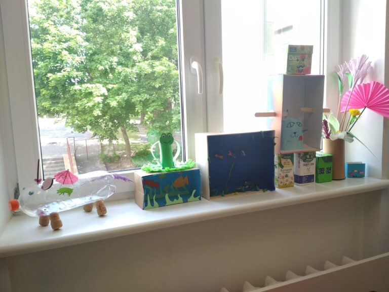 Przedstawia formy przestrzenne, w których wykorzystano surowce wtórne. Ustawione są one w formie wystawki, od prawej strony: akwarium, wazon z kwiatami, domek, robot, kot, 2 akwaria, żaba.