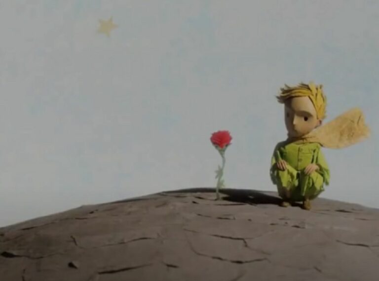Kadr z filmu "Mały Książę". Na zdjęciu Mały Książę siedzący obok czerwonej Róży.
